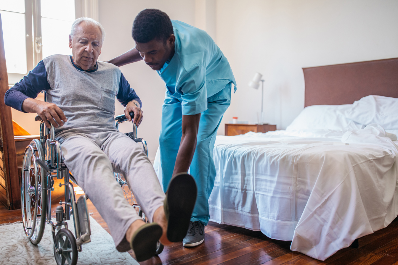 Man nurse helping senior in wheelchair in nursing home